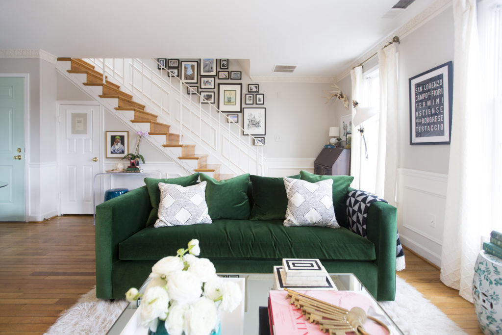 A beautiful apartment in Washington, DC. There is a dark green velvet couch as the centerpiece in the middle, and lots of art and flowers as decor.